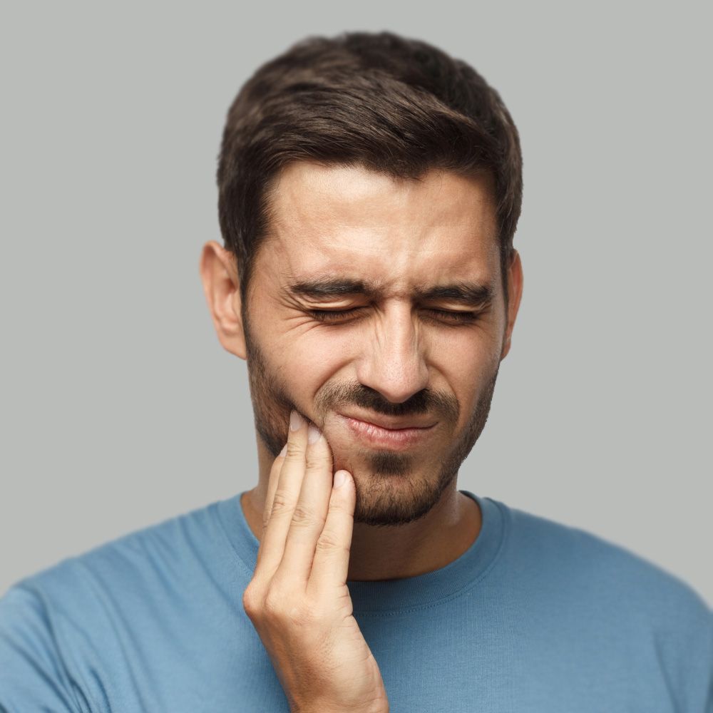 A man with his hand to his cheek, grimacing in pain